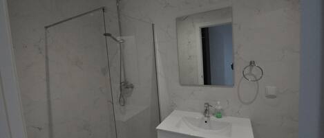 Ein modernes Badezimmer mit einer Duschkabine aus Glas, einem weißen Waschbecken und einem Spiegel darüber.