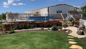 A fenced outdoor area with a pool, a building with a red roof, and a clear blue sky.