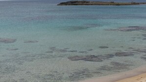 Una playa con agua turquesa cristalina, una orilla arenosa y un promontorio rocoso a lo lejos.