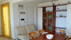 Un comedor con una mesa de madera, cuatro sillas, un sofá beige y un mueble con puertas de cristal.