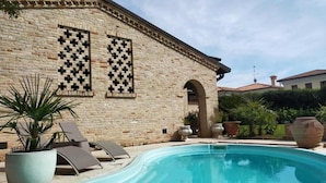 A pool area with a stone building, a checkered window pattern, and lounge chairs. - Damabianca junior (Porto Gruaro)
