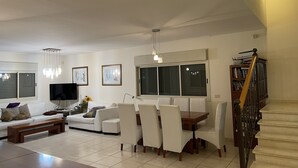 Un soggiorno moderno con un divano bianco, un tavolo da pranzo con sedie, una televisione e opere d'arte alle pareti.