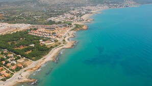 Vue aérienne d’une ville côtière avec une plage, des zones résidentielles et un paysage montagneux en arrière-plan.