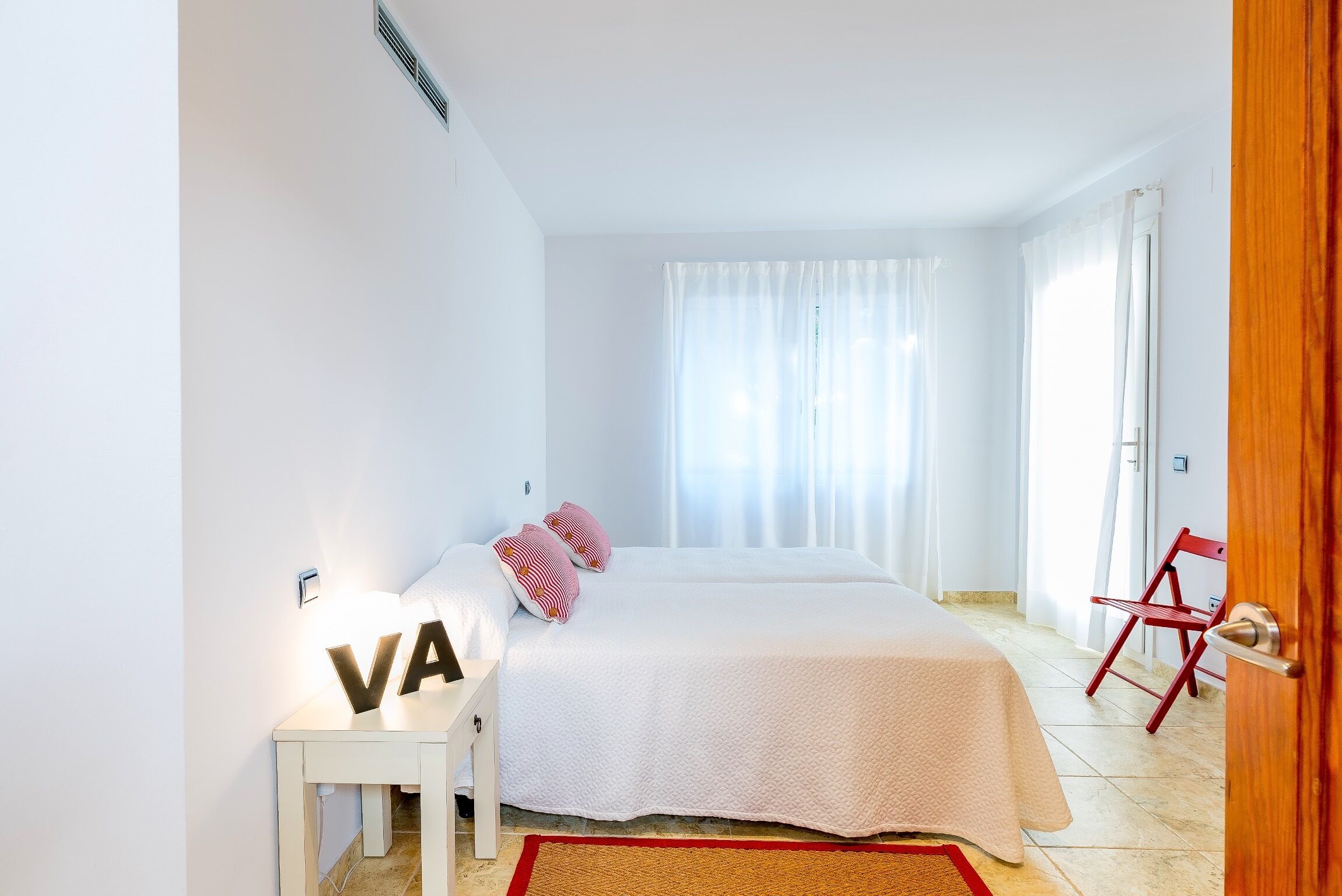 Ein Schlafzimmer mit einem Bett, einem Nachttisch, einem roten Sessel und einer Tür.