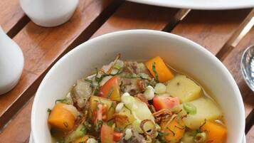 A bowl of stew with vegetables and meat, a plate of white rice, and two salt shakers on a wooden table.