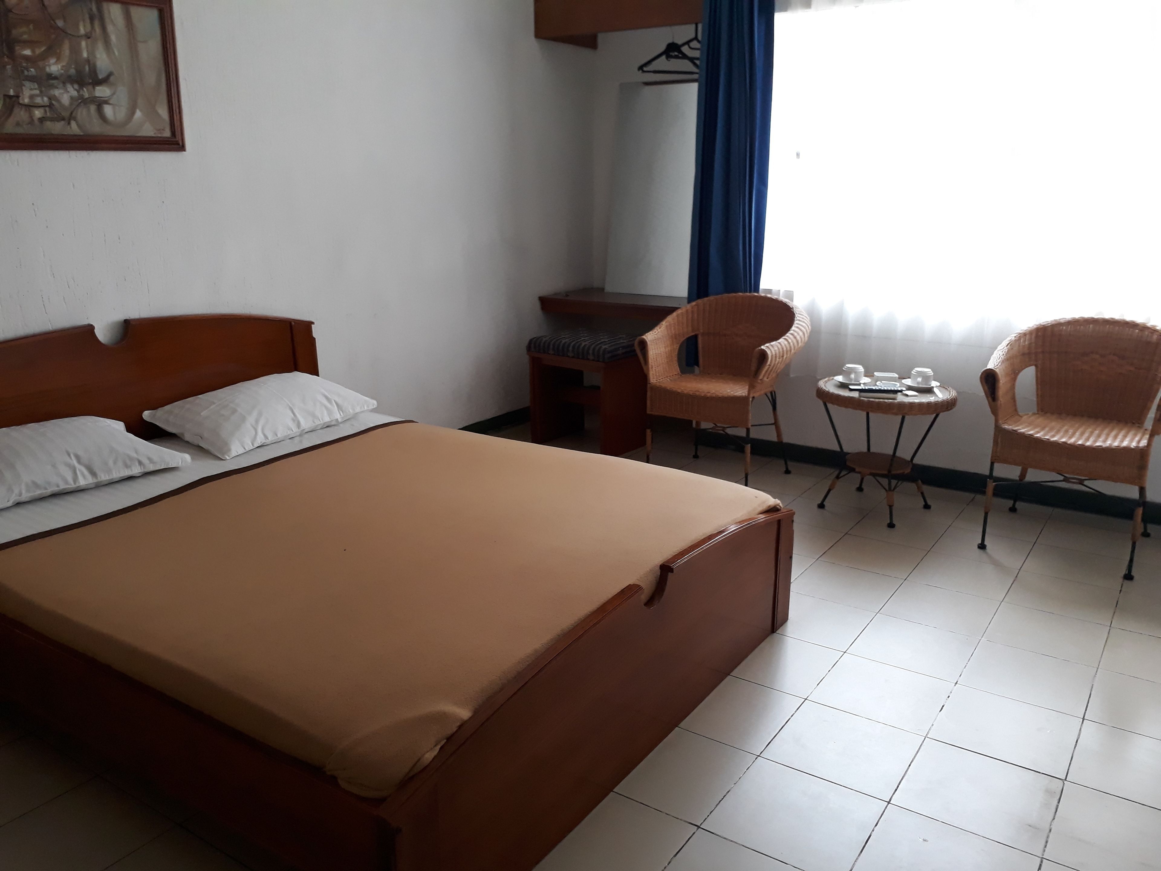 Quarto de hotel com uma cama, duas cadeiras, uma mesa pequena e uma escrivaninha.
