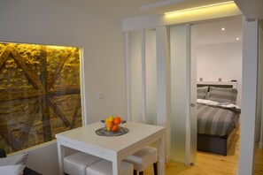 A modern room with a white table, a fruit bowl, and a bed with striped bedding.