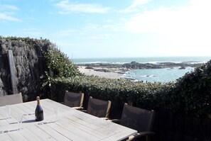 A table with a bottle and glasses, overlooking a rocky beach and ocean. - Seafront house with terrace on coastal path. 100 metres walk to beach (Piriac-sur-Mer)