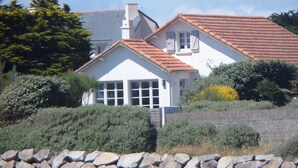 Une maison avec un toit recouvert de tuiles rouges, des murs blancs et un mur de pierre au premier plan.