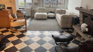Un salon avec un sol à carreaux, un canapé, un fauteuil et une cheminée.
