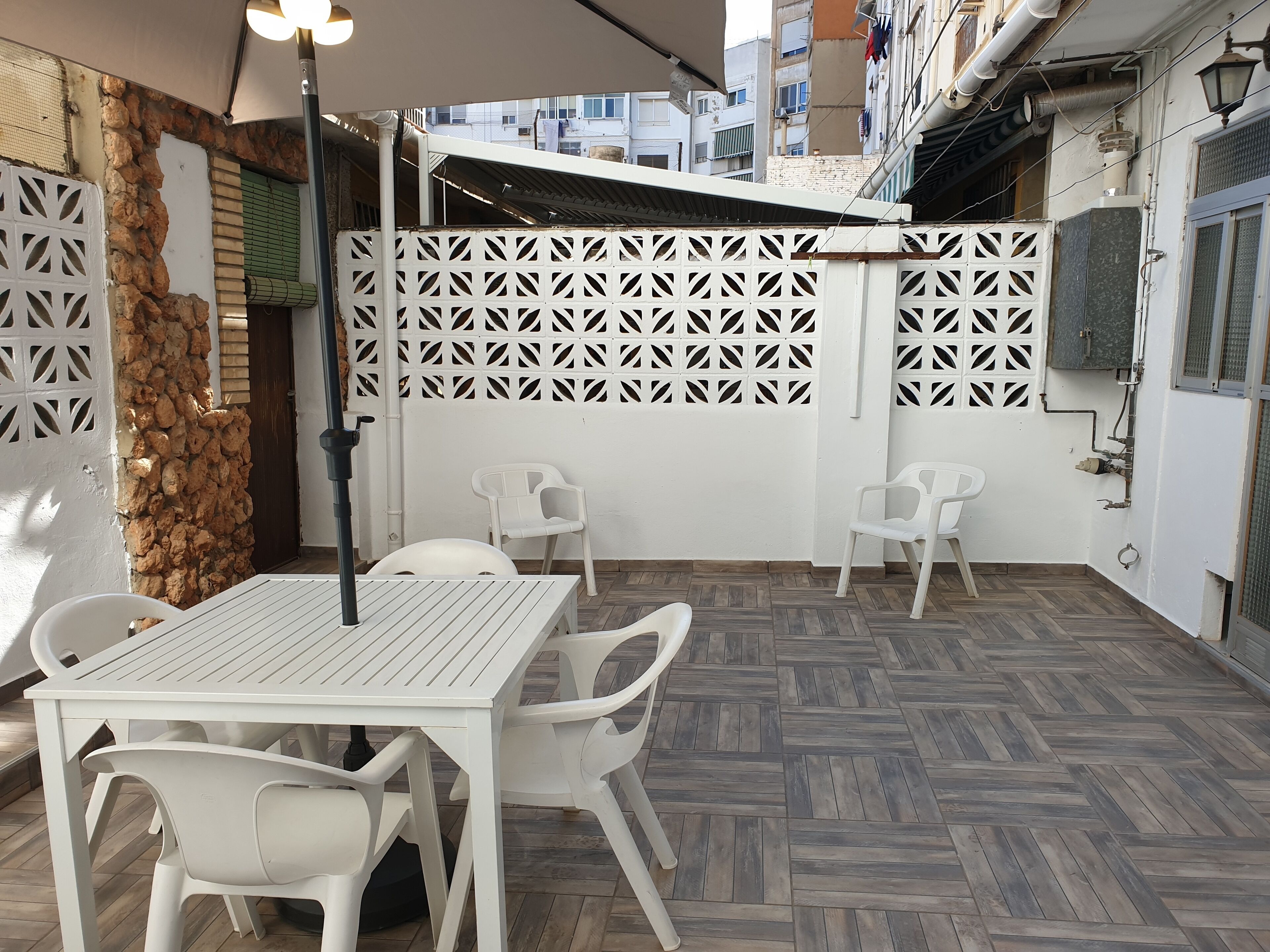 Un patio al aire libre con una mesa y sillas blancas, una cerca decorativa y una pared de piedra.
