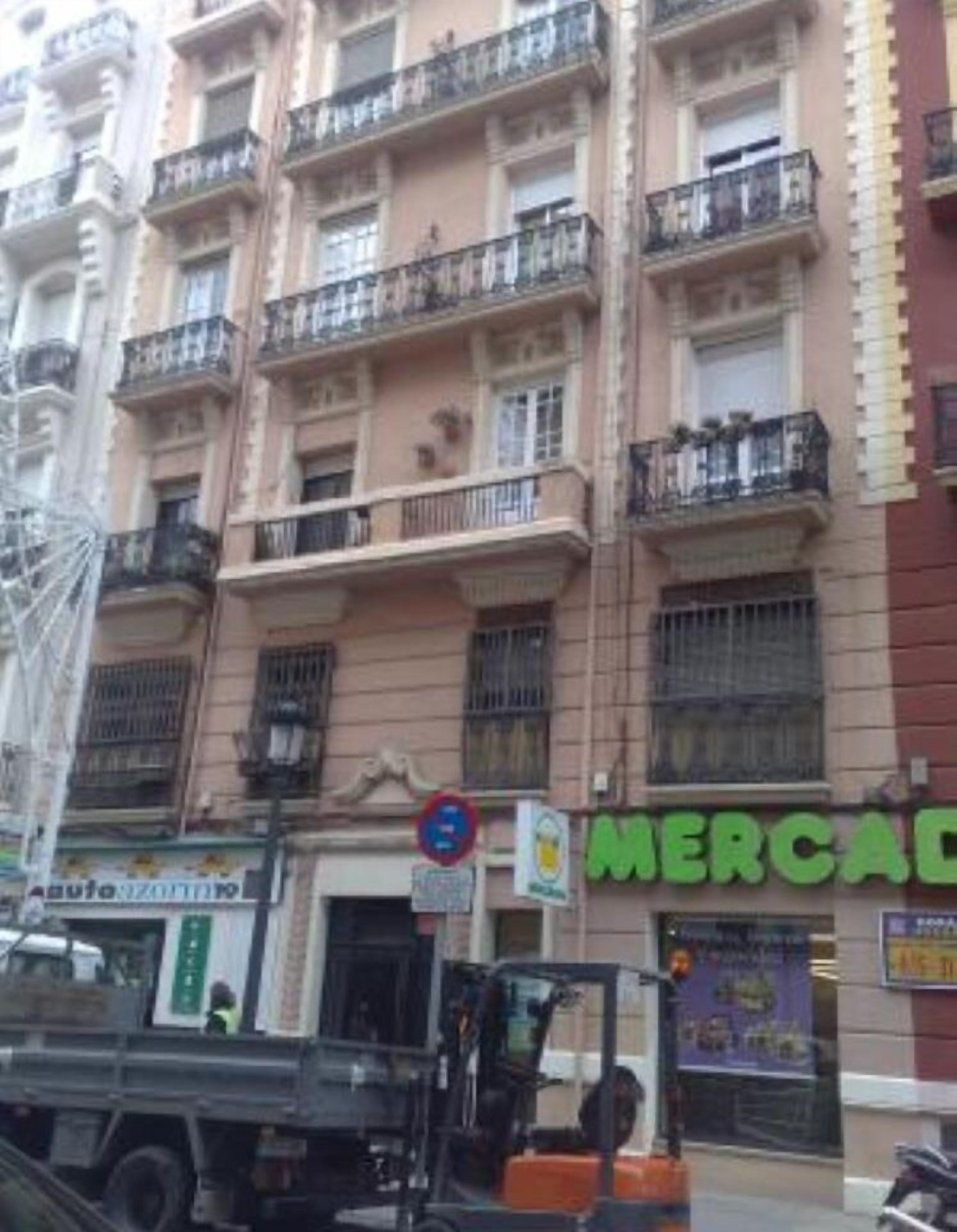 A multi-story building with balconies, a visible storefront with a green sign, and a parked truck.