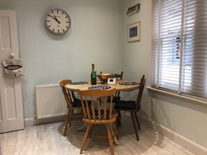 A dining area with a round table, wooden chairs, a clock, a bottle of champagne, and a framed picture on the wall.