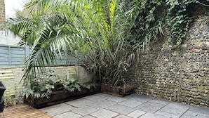 Un patio con piso de piedra, una terraza de madera y diversas plantas, incluyendo una palmera grande.