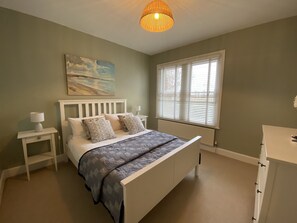 A bedroom with a bed, bedside tables, a lamp, a painting, a window with blinds, and a radiator.