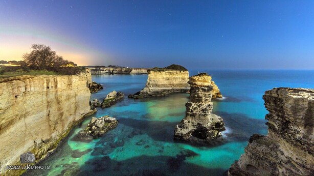 A coastal landscape with clear waters, rocky formations, and a rainbow.