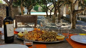 An outdoor dining area with a table set for a meal, including seafood and a bottle of wine.