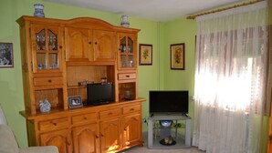 Ein Wohnzimmer mit einem Holzkabinett, einem Fernseher auf einem Schrank und einem Sofa.