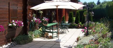A wooden cabin with a patio area featuring a table and chairs, surrounded by potted plants and flowers.