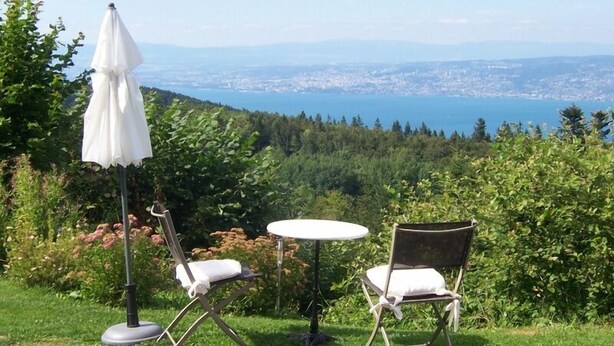A table and two chairs set up on a grassy hill overlooking a city and a body of water.