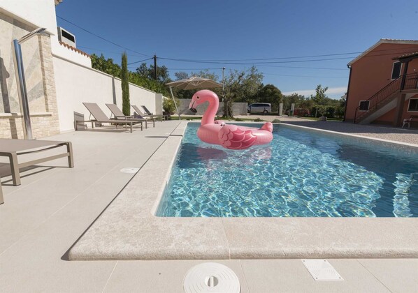 Una piscina con un flotador con forma de flamenco rosa, sillas de descanso y un área de patio cubierta.