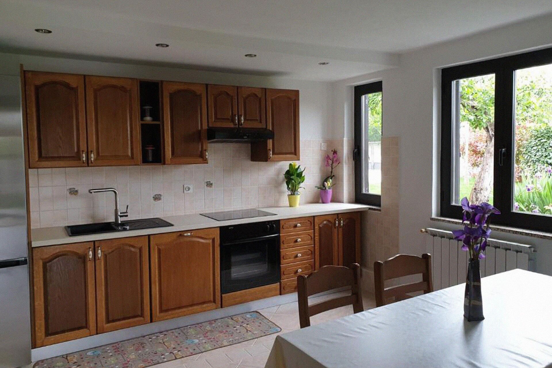 Une cuisine moderne avec des meubles en bois, un four encastré et une fenêtre donnant sur un paysage verdoyant.