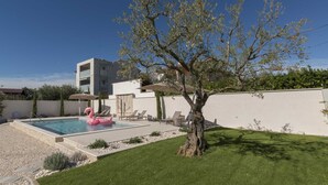 Une maison moderne avec une piscine, un flotteur en forme de flamant rose et un arbre dans le jardin.