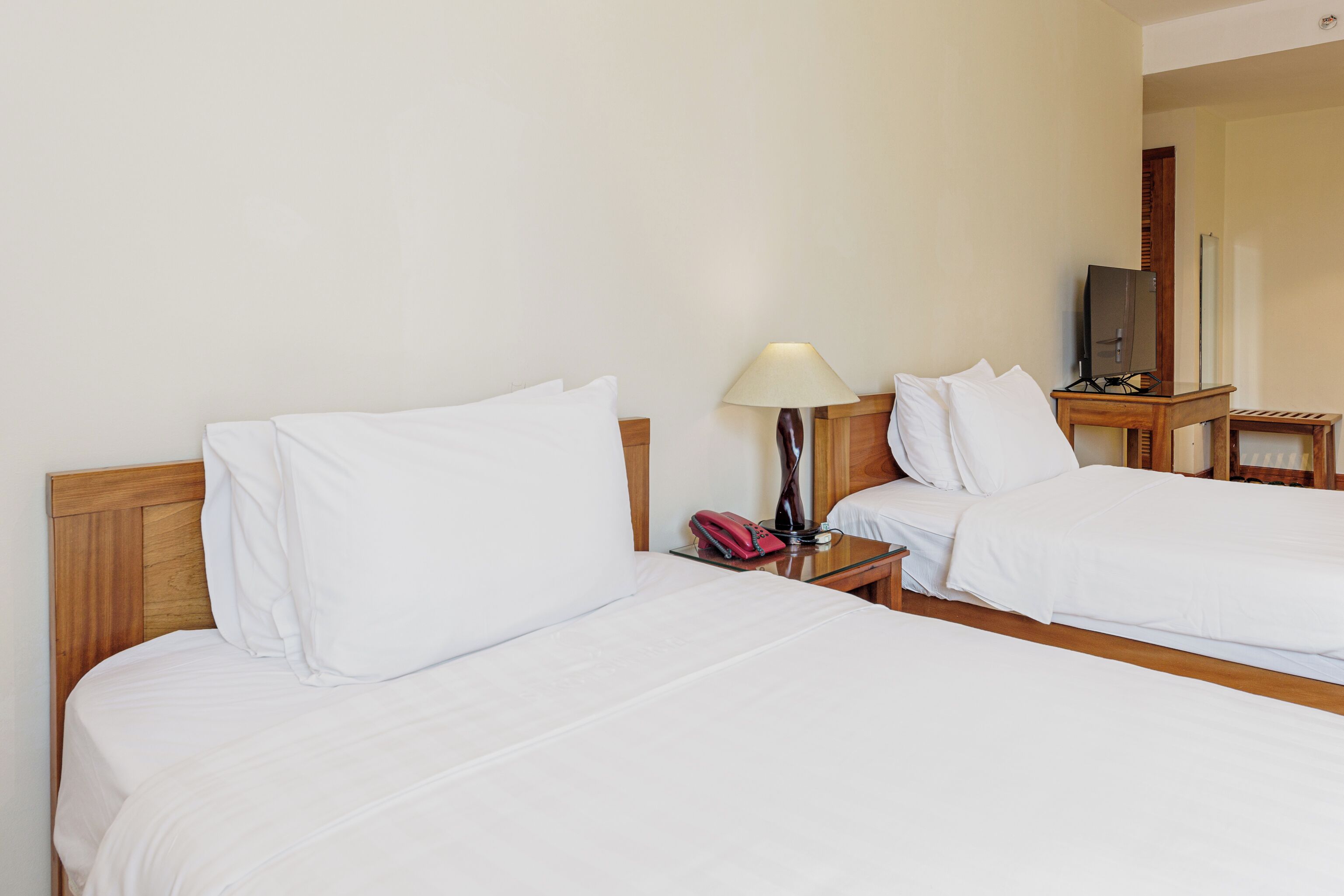 A hotel room with two single beds, a bedside table with a lamp, a telephone, and a TV on a small table.