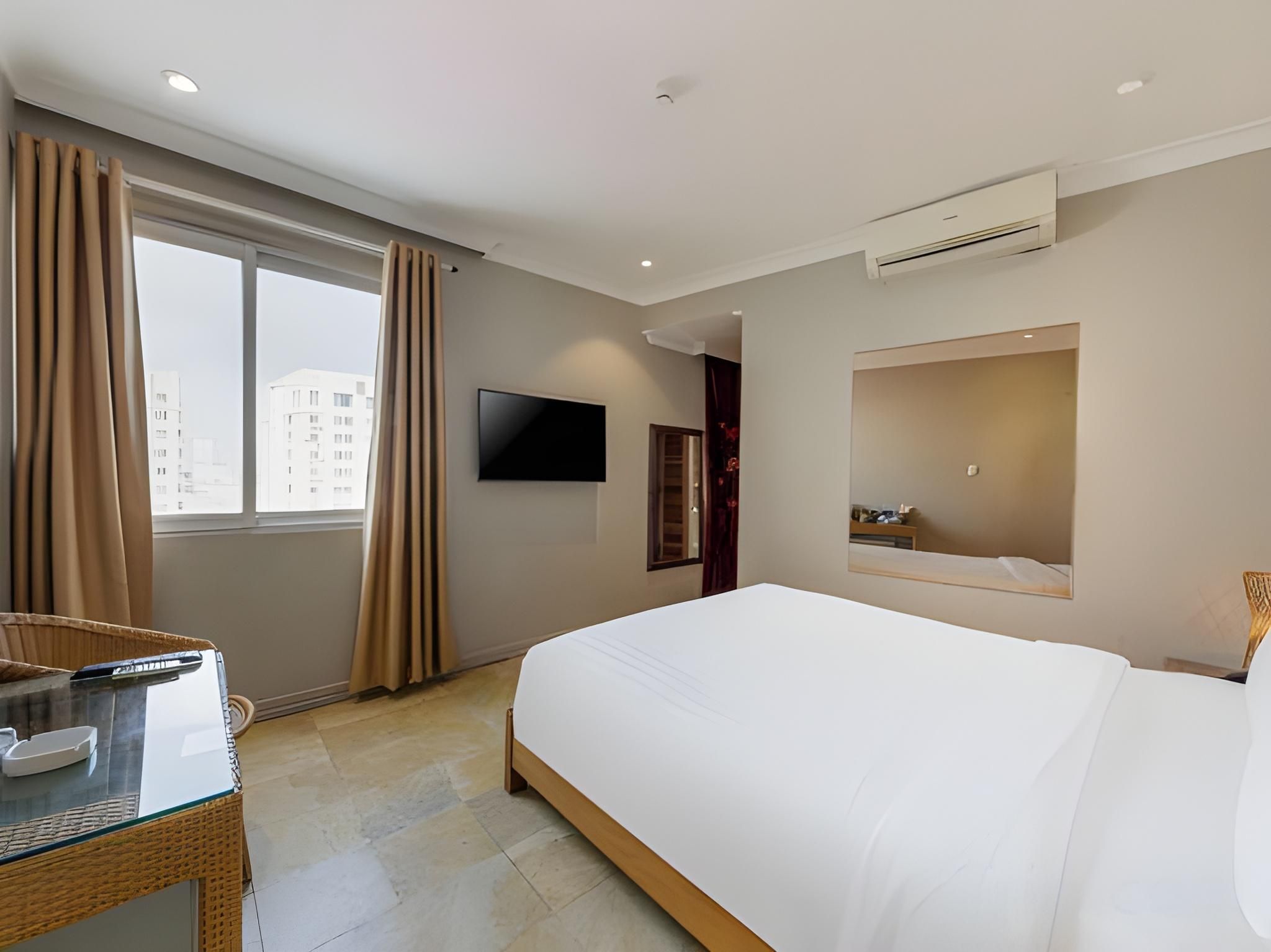 Une chambre d’hôtel dotée d’un grand lit, d’un téléviseur à écran plat fixé au mur, d’une fenêtre avec des rideaux et d’un appareil de climatisation.