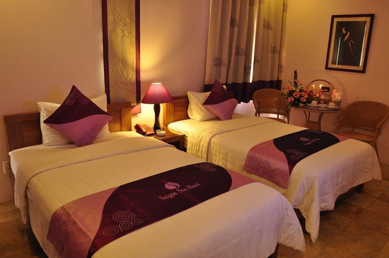 A hotel room with two beds, a nightstand, a lamp, a chair, and a small table with a vase of flowers.