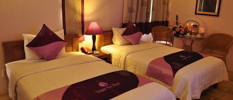A hotel room with two beds, a nightstand, a lamp, a chair, and a small table with a vase of flowers.