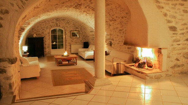 A cozy stone-walled living room with a fireplace, white furniture, and a tiled floor. - Luxury house in 15 acres of land with large private pool (Monteils)