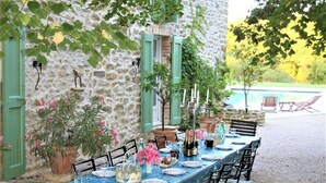 An outdoor dining area with a stone wall, green shutters, and a pool in the background. - Luxury house in 15 acres of land with large private pool (Monteils)