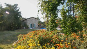 A stone building with a green door, surrounded by a garden with various flowers. - Luxury house in 15 acres of land with large private pool (Monteils)