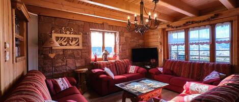 A cozy log cabin interior with a stone wall, wooden ceiling, and large windows.