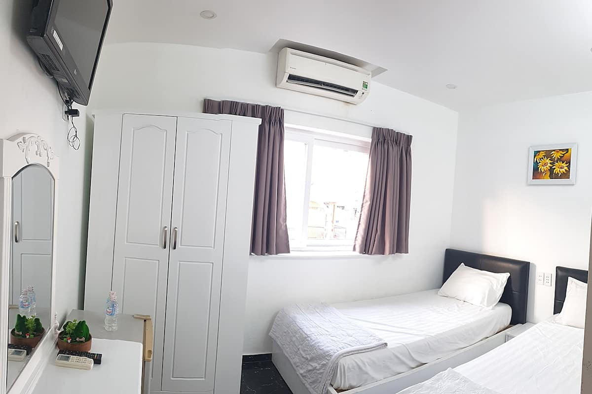 Une chambre d’hôtel comprenant un lit, une armoire, un bureau avec un miroir, une fenêtre avec des rideaux, un climatiseur et un téléviseur fixé au mur.