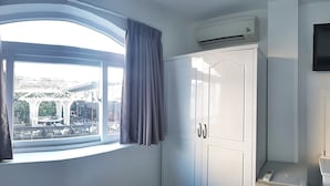 A room with a large window, a wardrobe, an air conditioning unit, and a television.