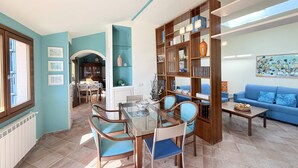 Un comedor con mesa y sillas de vidrio, una estantería de madera y un sofá azul.
