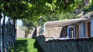 Un muro de piedra con una cerca de metal y un sendero que conduce a un edificio con contraventanas azules.