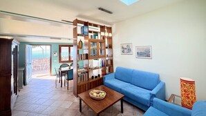 Amplia sala de estar con un sofá azul, una mesa de centro de madera con fruta, una estantería y un tragaluz.