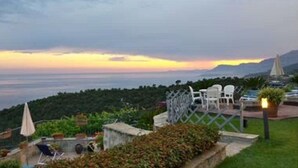 Una terraza con mobiliario exterior, con vistas a un paisaje costero al atardecer.