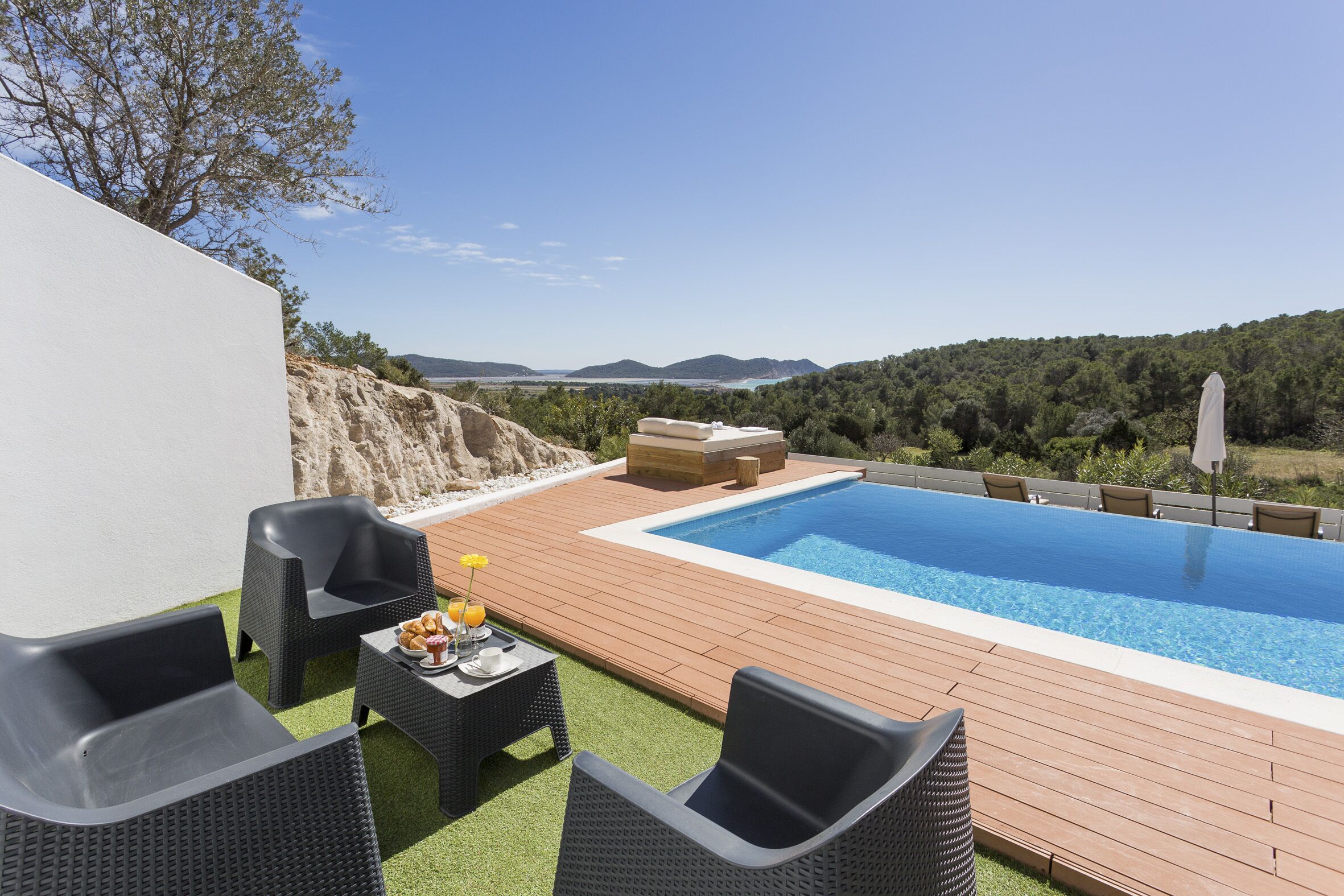 An outdoor swimming pool with a wooden deck, wicker furniture, and a table with drinks.