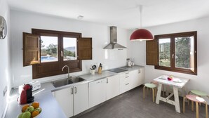 A modern kitchen with white cabinets, a stainless steel sink, a red pendant light, and a view of the outdoors through large windows.