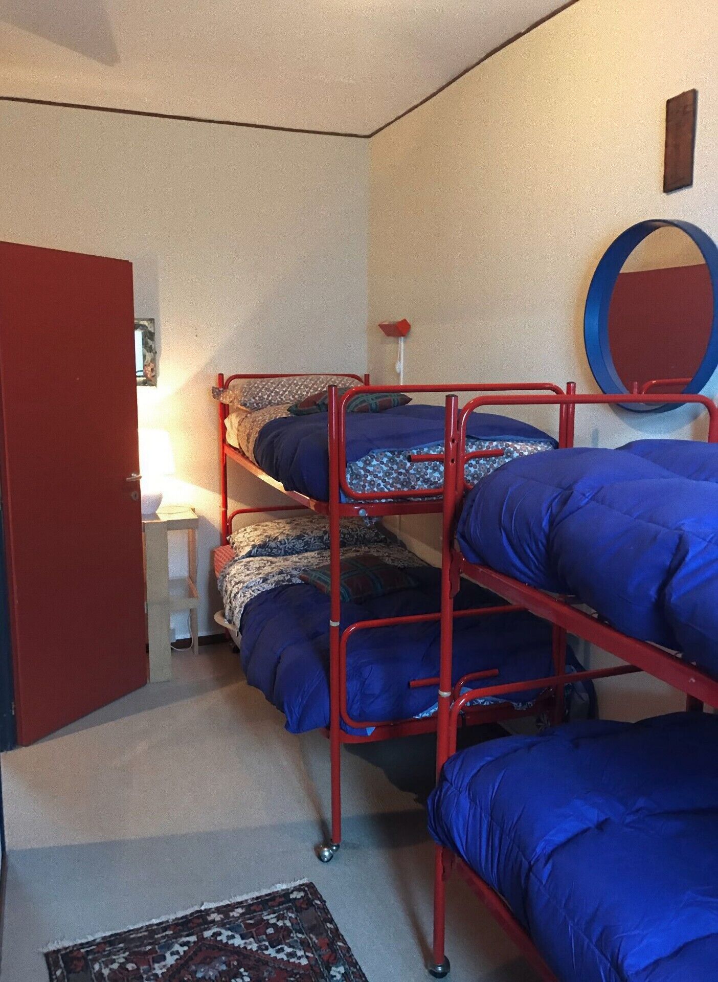 Asuntolan huone, jossa on kerrossängyt, pieni pöytä, lamppu ja peili seinällä.