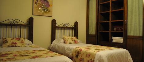 Dos camas individuales con ropa de cama floral, un armario de madera con puertas de cristal y un cuadro en la pared.