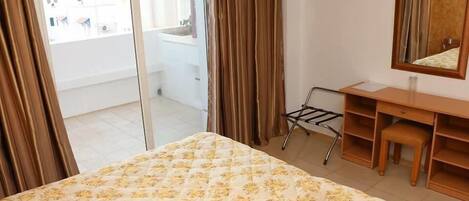 Habitación de hotel con cama, escritorio, silla, espejo y vista al balcón exterior.