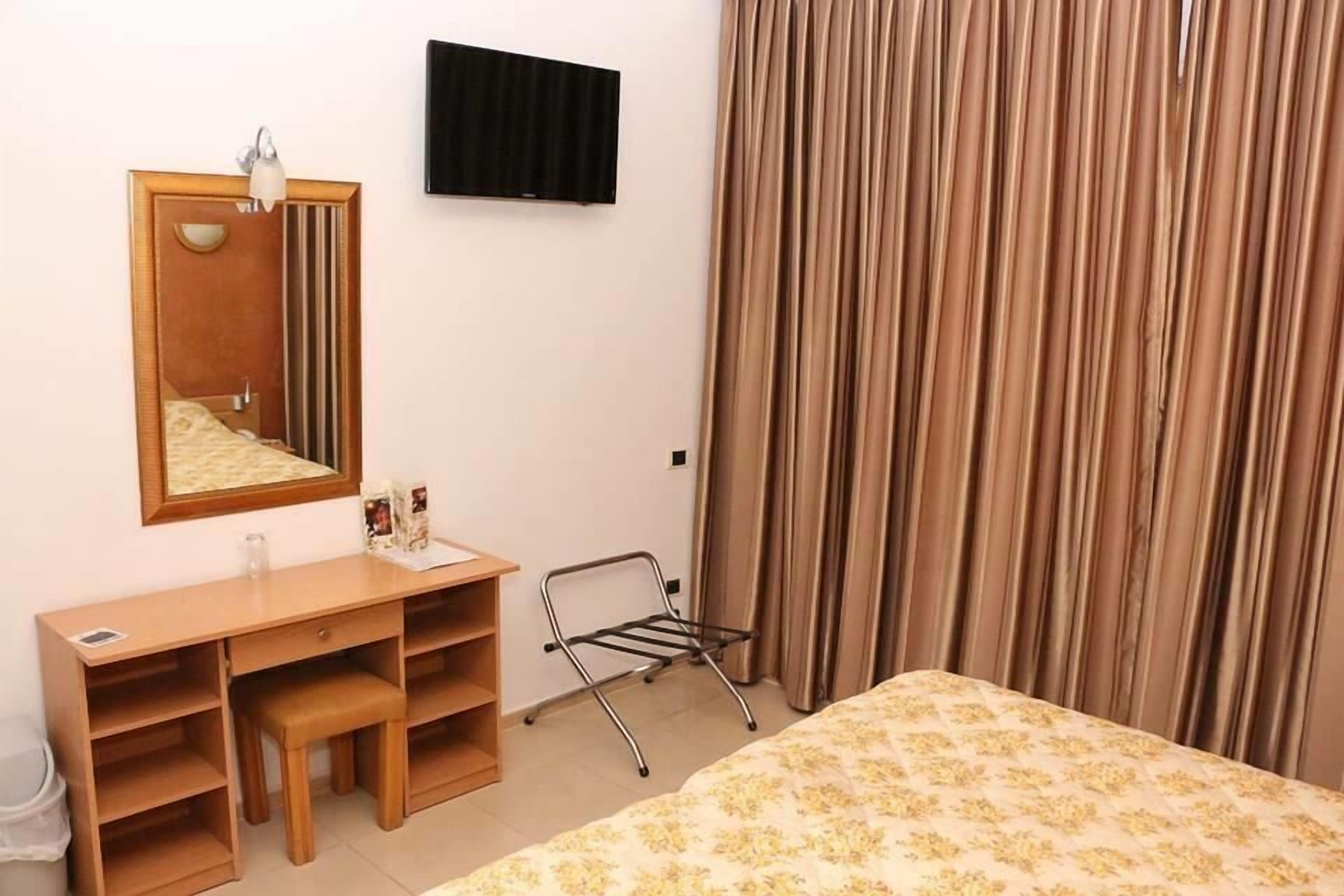 Habitación de hotel con cama, escritorio, silla, espejo, televisor y ventana con cortinas.