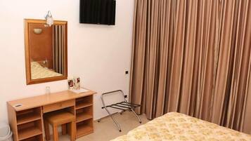 Habitación de hotel con cama, escritorio, silla, espejo, televisor y ventana con cortinas.