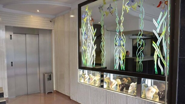 A hallway with an elevator, a glass display case with jewelry, and a decorative wall with abstract patterns. - Hotel Yasmine (Sfax)