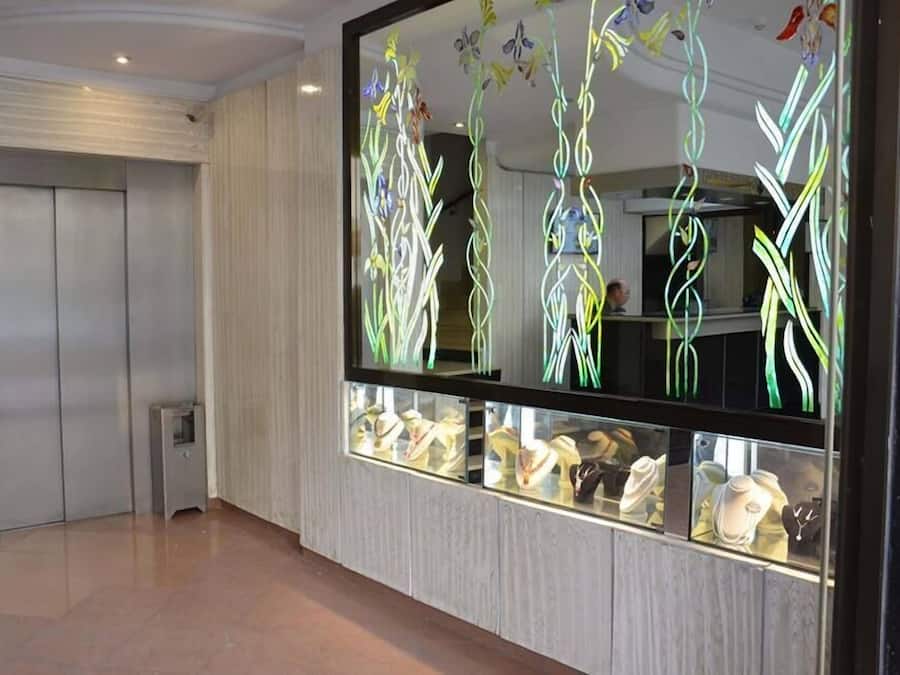 Un couloir avec un ascenseur, une vitrine en verre contenant des bijoux et un mur décoratif orné de motifs abstraits.